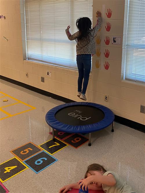 Girl jumping on floor trampoline to tap a decal higher up on the wall.